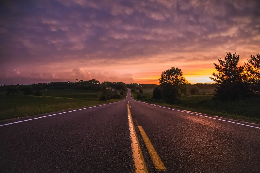 Camino recto al atardecer entre terrenos planos (foto referencial)